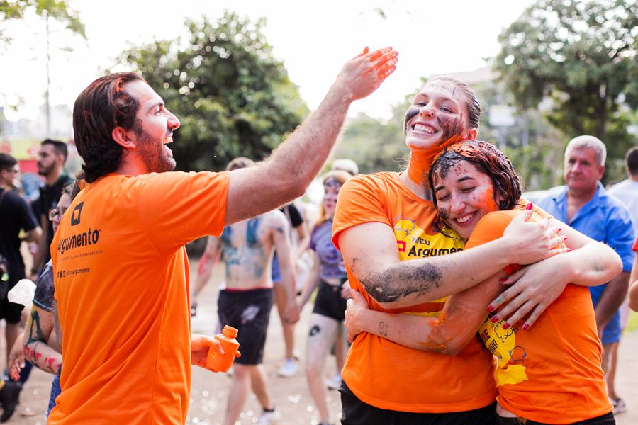 Professor da Argumento comemora com duas alunas aprovadas que se abraçam, pintadas de laranja no trote