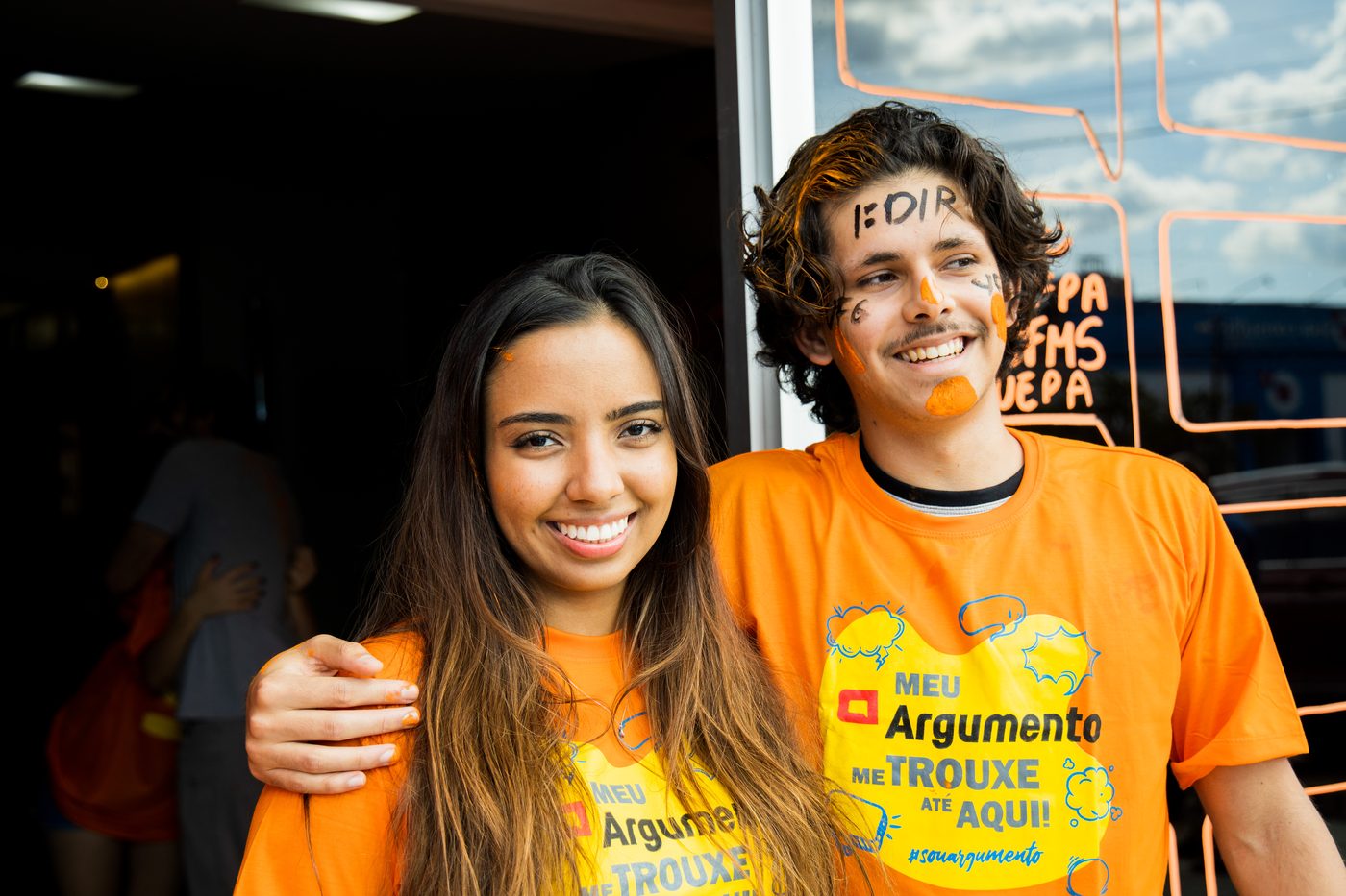 Aluna e aluno aprovados abraçados na porta da escola