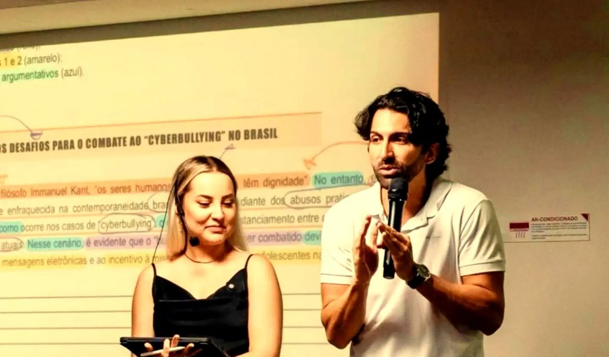 Raphaella Paiva e Antonio Marcos em aula, diante de uma redação projetada com trechos marcados em cores