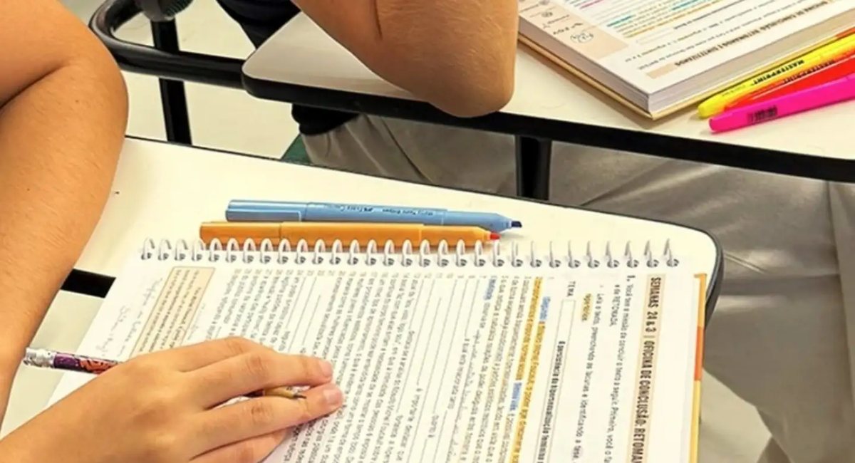 Livro aberto sobre a carteira, com trechos marcados em cores e canetas marca-texto ao lado